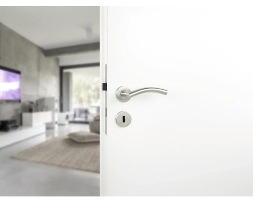 Witte binnendeur met deurklink en sleutelgat die naar een moderne woonkamer leidt