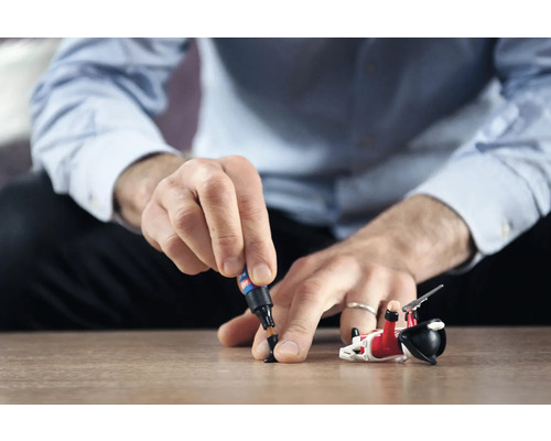 Man repareert speelgoedfiguur met lijm op tafel