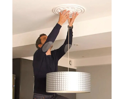 Man installeert een plafondrozet en een hanglamp aan het plafond.