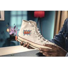 Persoon houdt witte Converse sneaker met comic patch in de hand