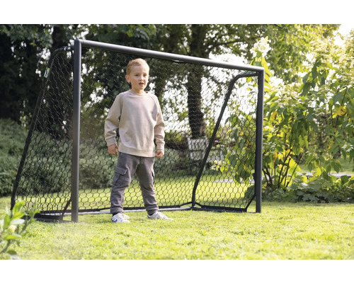 Een jongen staat voor een voetbaldoel in de tuin.