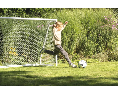 Jongen schiet voetbal voor een voetbaldoel in de tuin