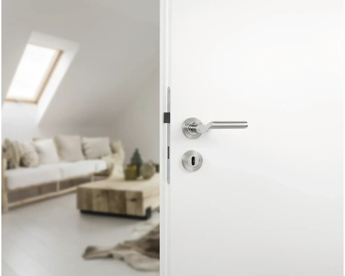 Witte binnendeur met zilverkleurige deurklink naar een lichte woonkamer