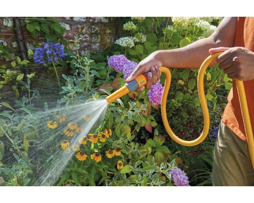 Persoon besproeit bloemen in de tuin met een tuinslang.