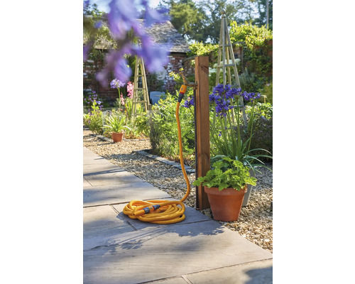 Tuinscene met een gele tuinslang aangesloten op een waterkraan in de tuin