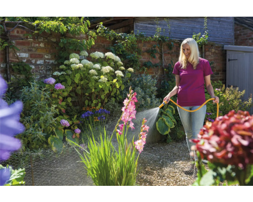 Vrouw besproeit bloemen met een tuinslang in de tuin.