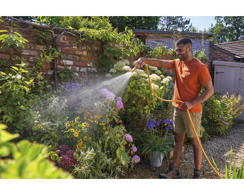 Man besproeit tuin met tuinslang en diverse bloemen