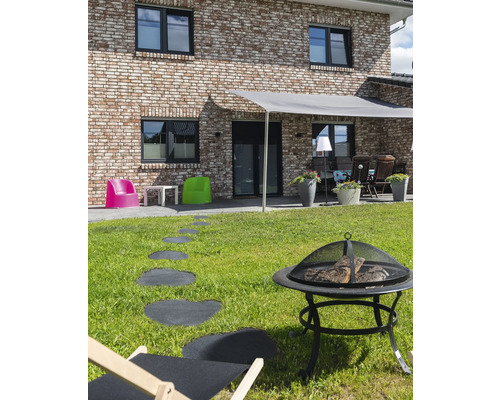 Buitenruimte met vuurplaats, ligstoel, stapstenen en zonwering voor een woonhuis