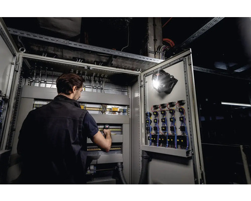 Elektricien aan het werk aan een schakelkast met lamp bevestigd