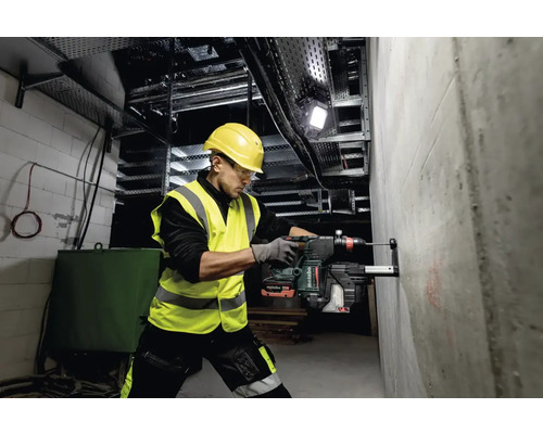 Een man boort met een boorhamer een gat in een betonnen muur op een bouwplaats.