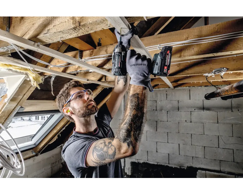 Ambachtsman werkt met een accuschroevendraaier aan een houten constructie, veiligheidsbril en gehoorbescherming worden gedragen.