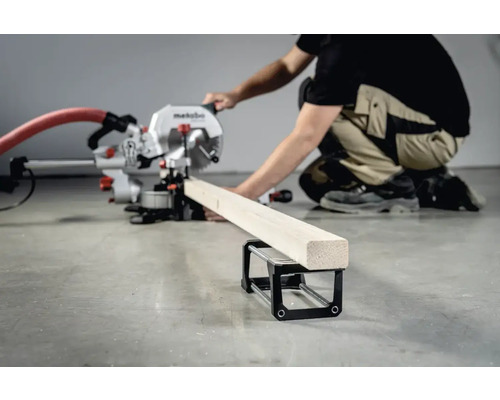 Een persoon bedient een afkortzaag om een stuk hout te zagen dat op een materiaaltafel ligt.