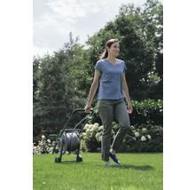 Vrouw duwt een tuinslangwagen in de tuin.