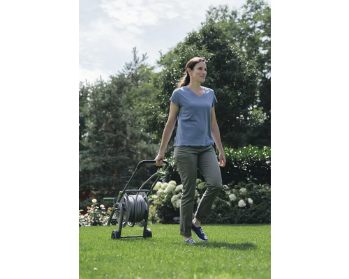 Vrouw duwt een tuinslangwagen in de tuin.
