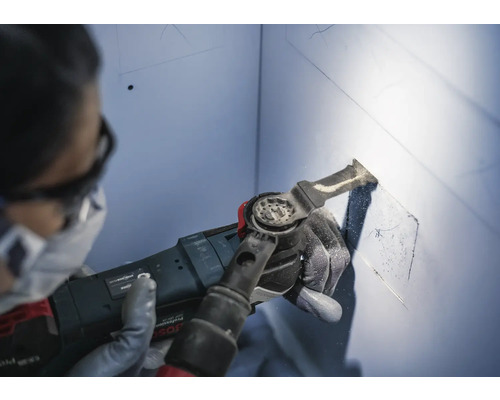 Een persoon gebruikt een multifunctioneel gereedschap om een uitsparing in een muur te snijden.