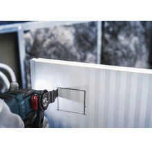 Een hand snijdt met een multifunctioneel gereedschap een rechthoek in een isolatieplaat.