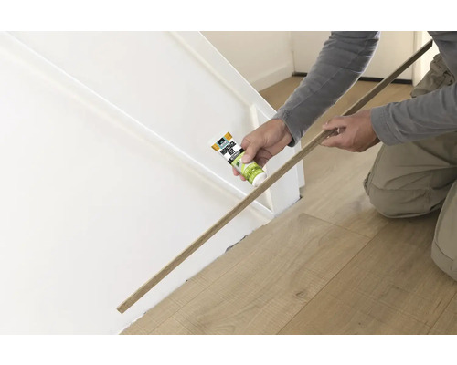 Een persoon bevestigt een houten lijst met montagekit aan een muur.