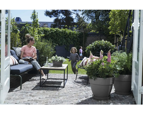 Scene van een tuin met een vrouw op een bank, spelende kinderen en beplante bloempotten.