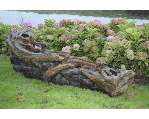 Tuinfontein met boomstamdesign en waterspel op gazon voor hortensiastruiken