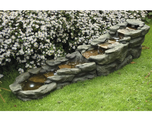 Meerlagige tuin fontein met steenlook, buiten op gazon voor een bloemenmuur