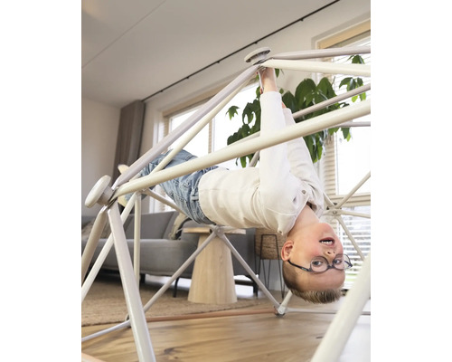 Jongen hangt ondersteboven aan een indoor klimrek in de woonkamer.