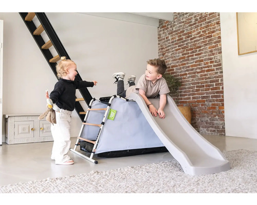 Twee kinderen spelen met een glijbaan met ladder voor binnenshuis in een woonkamer.