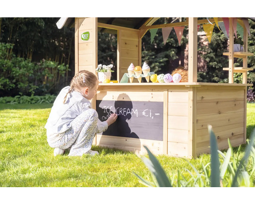 Meisje schrijft met krijt op een houten speelgoedwinkel in de tuin.