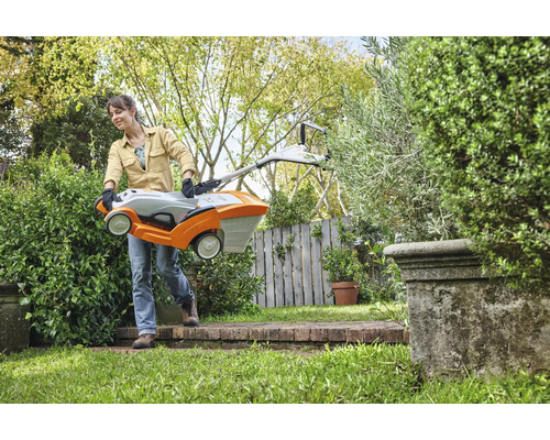 Een vrouw draagt een grasmaaier door een tuin.