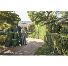 Man staat naast heggenschaar en volle tuinzakken voor een huis.