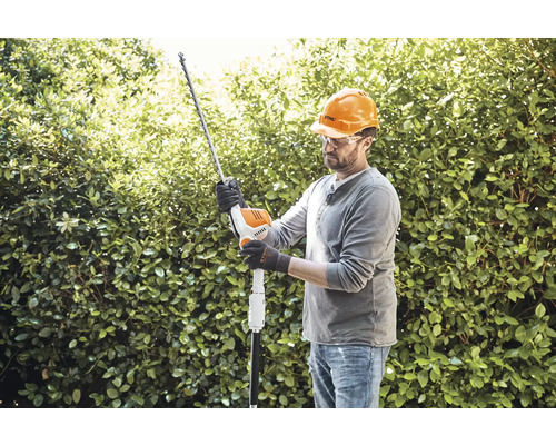 Man met veiligheidshelm en veiligheidsbril snoeit heg met heggenschaar.