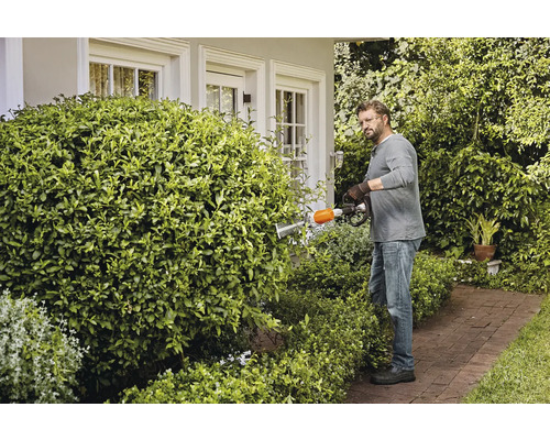 Een man snoeit een haag met een heggenschaar in een tuin.