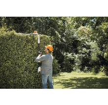 Een persoon snoeit een heg met een accuheggenschaar met telescopische steel.