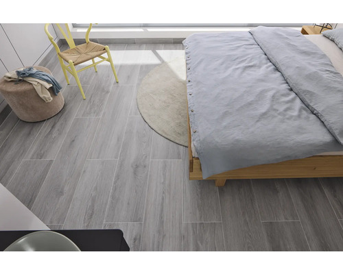 Slaapkamer met bed, stoel, kruk, tapijt en grijze houtlook vloertegels