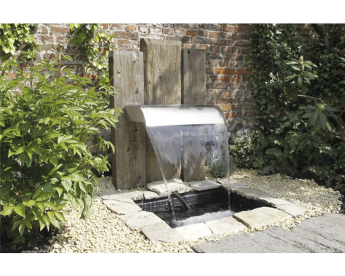 Tuinscene met roestvrijstalen waterval en houten elementen in een stenen vijver