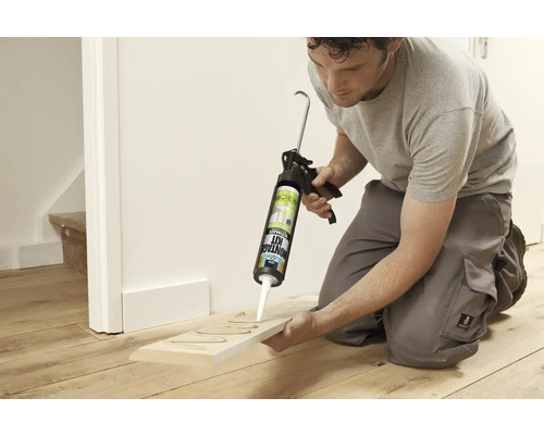 Een man gebruikt een kitpistool om lijm op een houten plank aan te brengen.