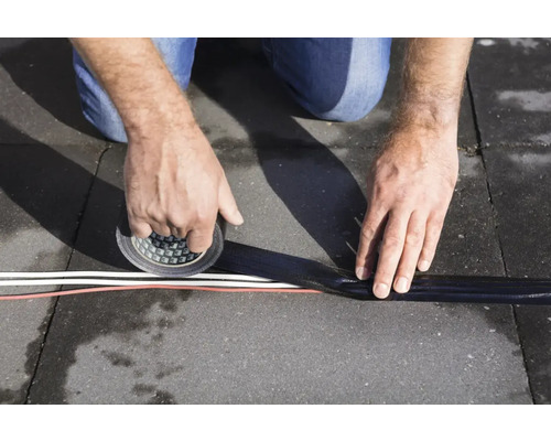 Een persoon repareert een kabel op de vloer met tape.