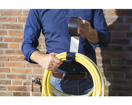 Een persoon houdt een gele tuinslang vast, omwikkeld met zwarte ducttape, en een rol ducttape.