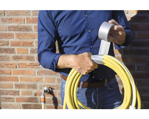 Een persoon repareert een gele tuinslang met ducttape.