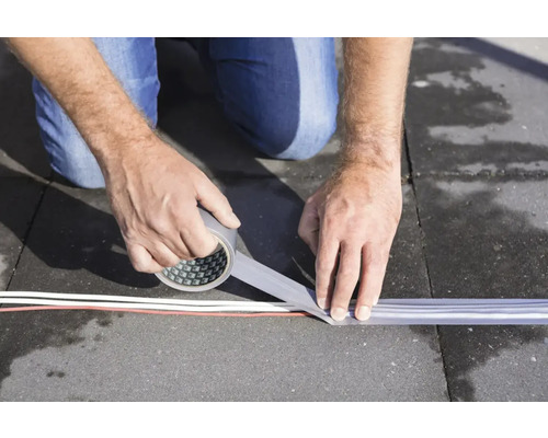 Een persoon bevestigt een kabelbeschermingsstrip met ducttape op een ondergrond.
