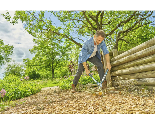 Een man snoeit takken met een takkenschaar in een tuin met een houten hek.