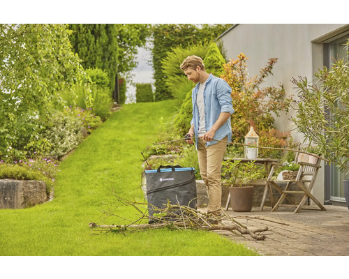 Man knipt tuinafval met een tuinschaar en een tuinzak in de tuin.