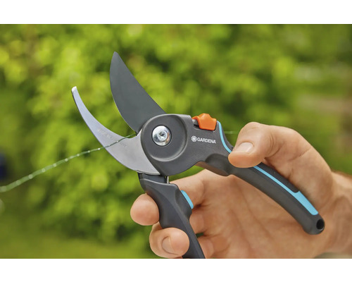 Een hand houdt een Gardena tuinschaar vast die een dunne tak doorknipt.