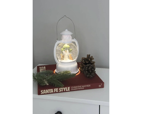 Decoratieve lantaarn met sneeuwbol, engel en kerstboom op een nachtkastje