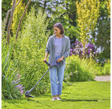 Vrouw snijdt gras met een grastrimmer in een tuin.