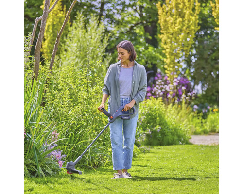 Vrouw snijdt gras met een grastrimmer in een tuin.