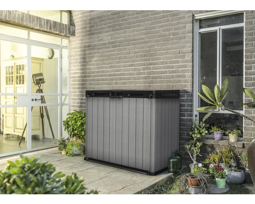 Kunststof tuingereedschapskast op een terras voor een bakstenen muur.