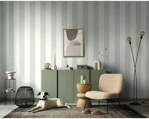 Woonkamer met gestreept behang, dressoir, fauteuil, staande lamp en hond