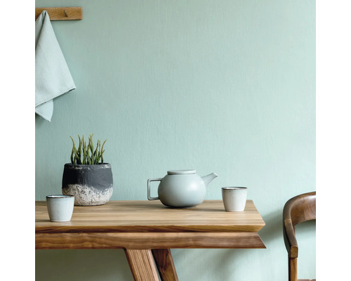 Houten tafel met theepot, kopjes en plant in pot voor een wand