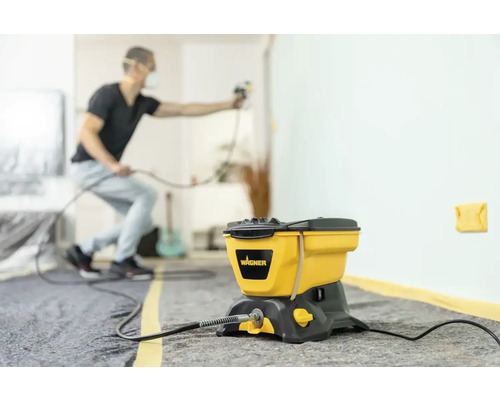 Verfspuitsysteem met een man die een muur binnenshuis spuit