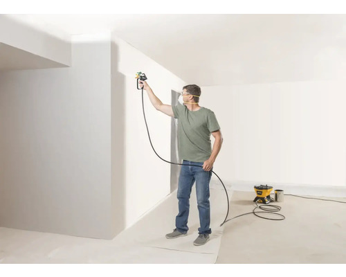 Man schildert muur met verfspuitsysteem in lichte kamer